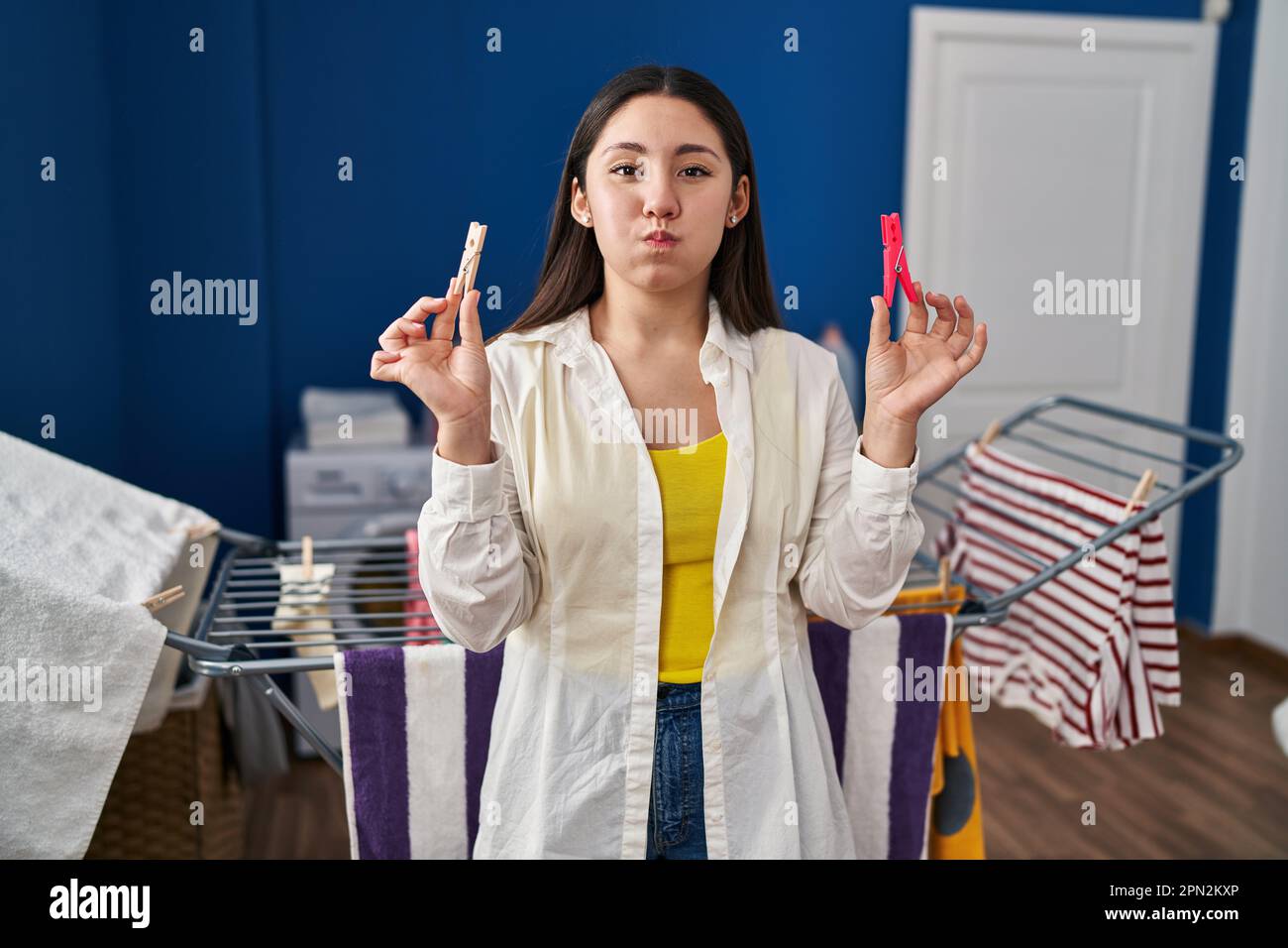 Young latin woman holding clothespins hanging clothes on clothesline