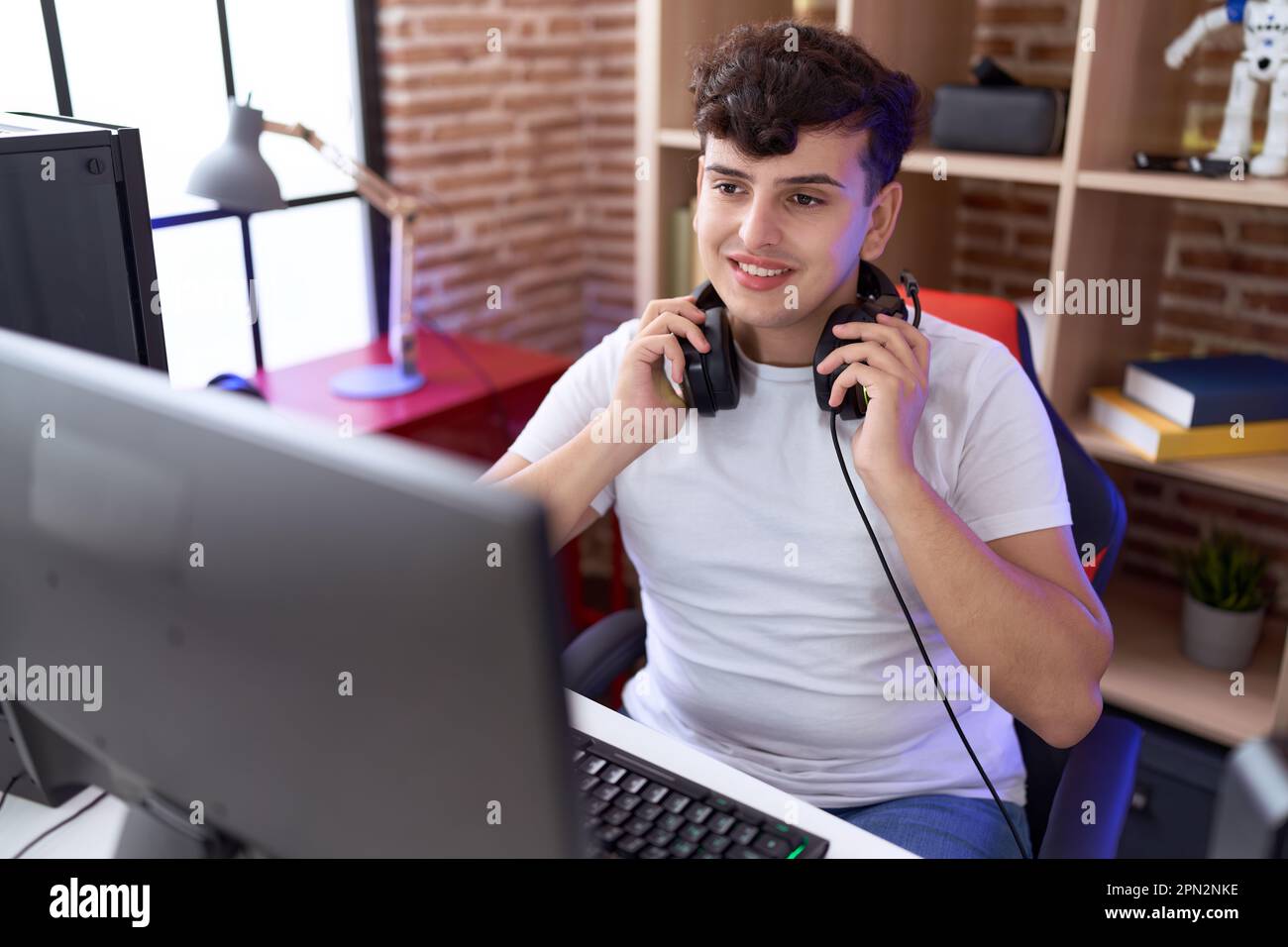 Non binary man streamer smiling confident sitting on table at gaming ...