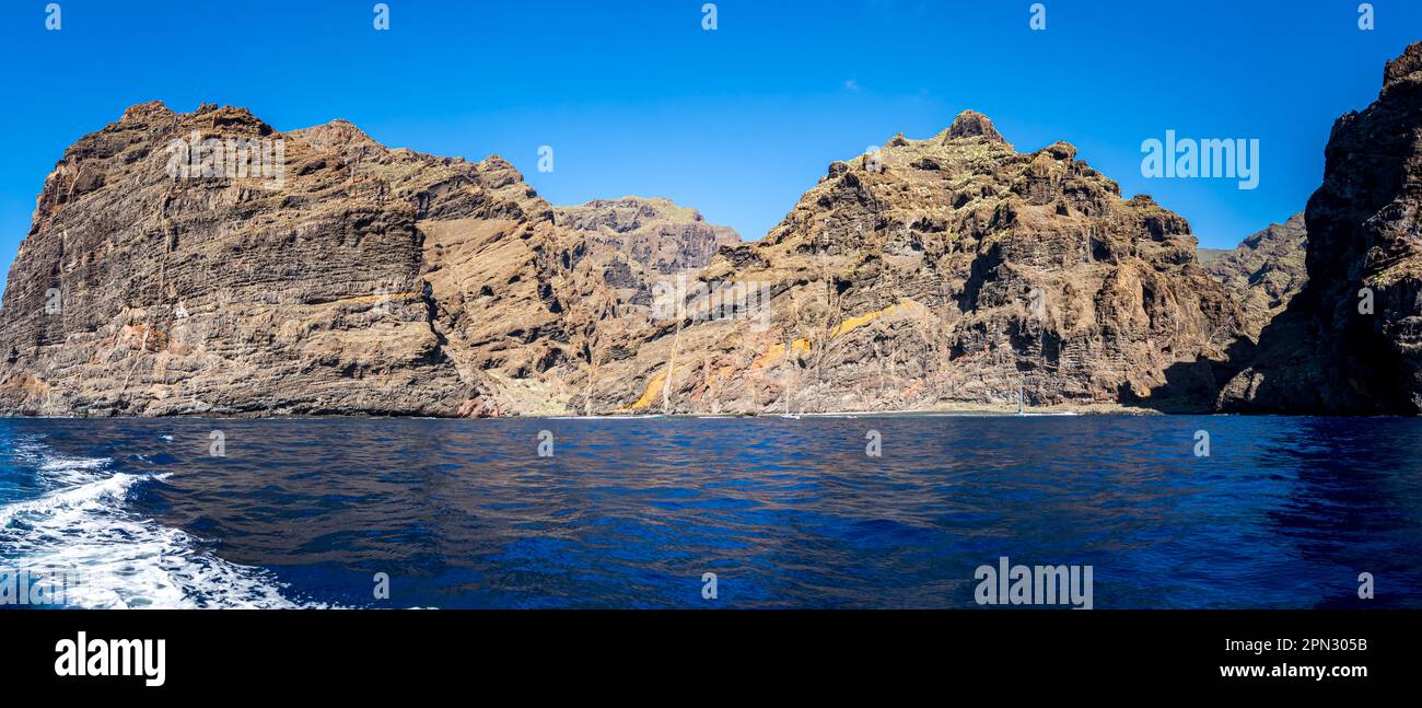 Panoramic view of the Playa de Barranco Seco beach nestled at the foot of Acantilados de Los Gigantes cliffs, with sailboats anchored in the calm sea. Stock Photo