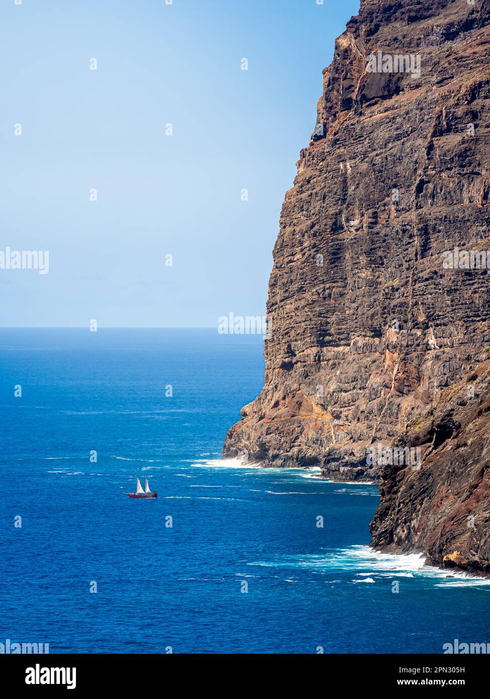 A pirate sailboat sets out on an adventure amidst the awe-inspiring cliffs of Los Gigantes, with the vast Atlantic Ocean stretching into the distance. Stock Photo