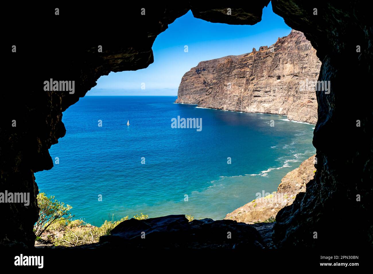 View upon waters of Los Gigantes Bay from the entrance of a small cave, with the imposing Acantilados de Los Gigantes cliffs towering above the sea. Stock Photo
