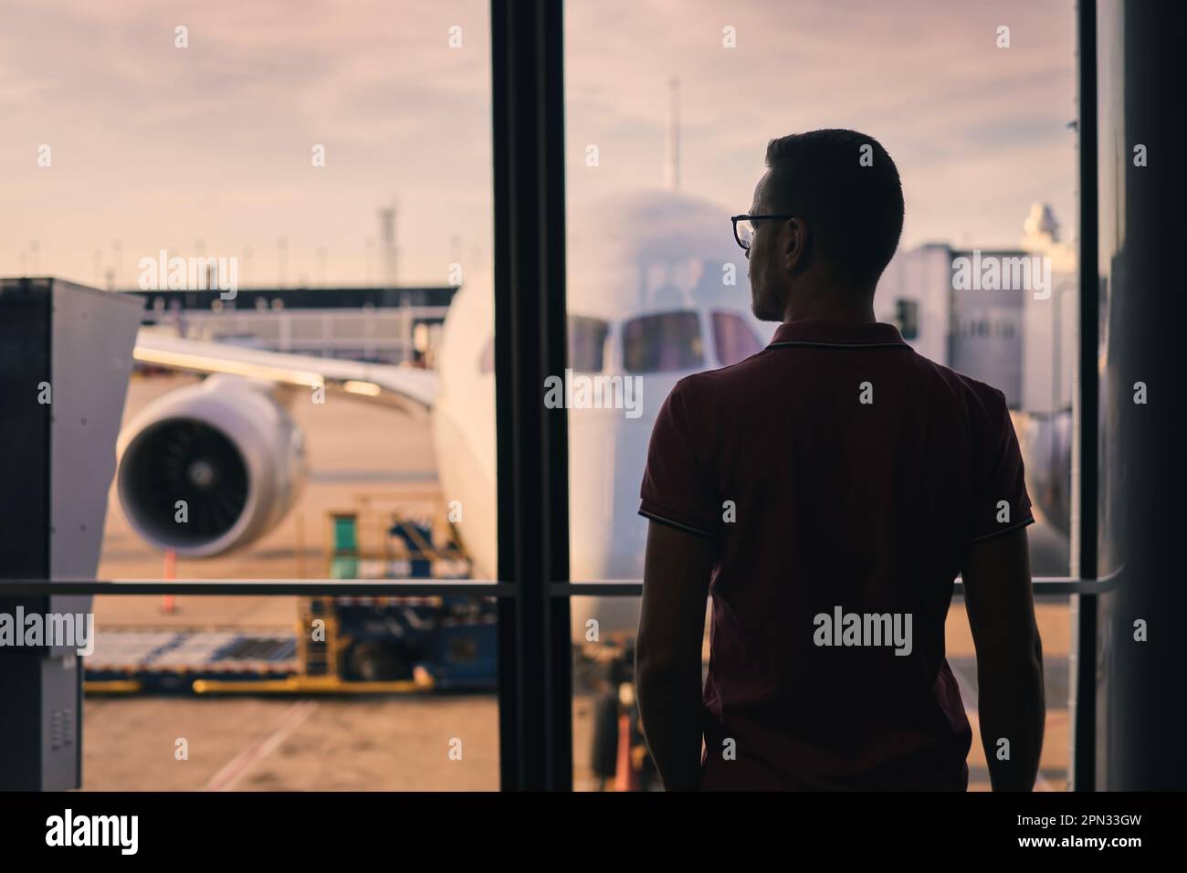 Traveler is looking out of airport window at airplane. Silhouette of man waiting for his flight. Stock Photo