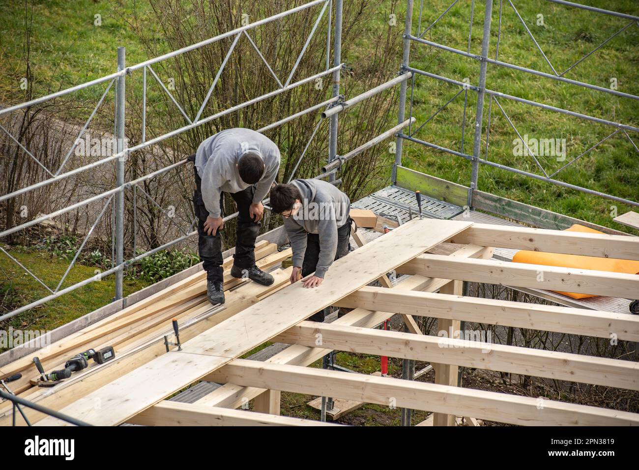 Two young carpenters building a carport. Apprentice learns from trainer. Stock Photo