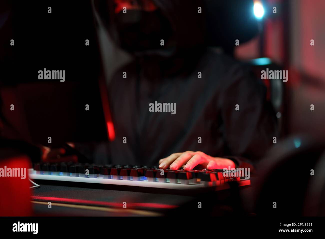 Hacker in hoodie working on computer and typing on keyboard to hacking programming system or server. Stock Photo