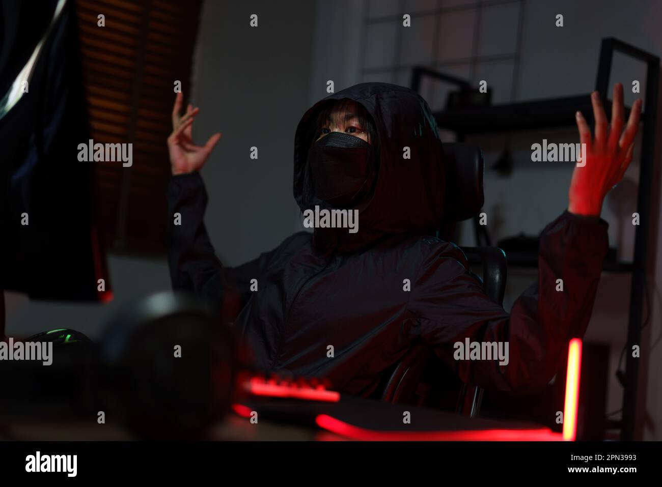 Hacker in hoodie raising hands while having problem with hacking programming system or server. Stock Photo