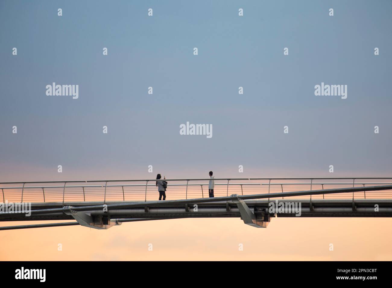 Young couple taking photos of each other on the Millennium Bridge London at sunset Stock Photo