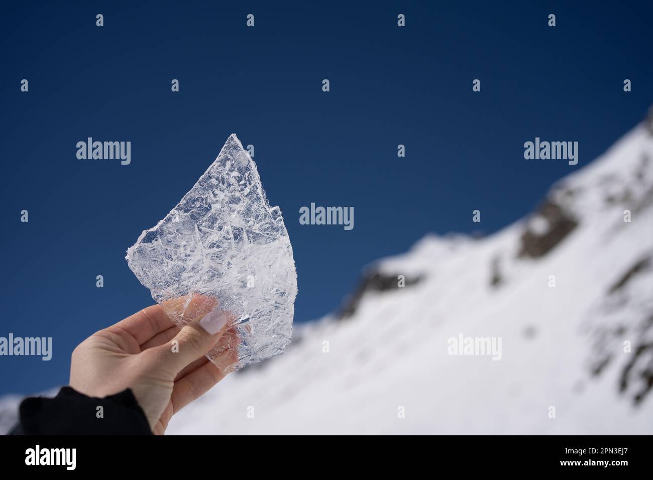 A beautiful piece of ice in a female hand against the blue sky and mountains Stock Photo