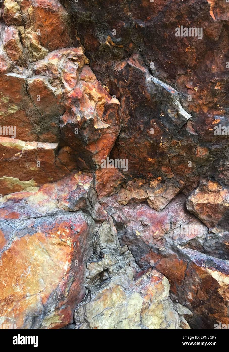 Rhyolite extrusive igneous rock formation. The colours come from the minerals: oxidised iron (orange/red/yellow), magnesium (black) and silica (white) Stock Photo
