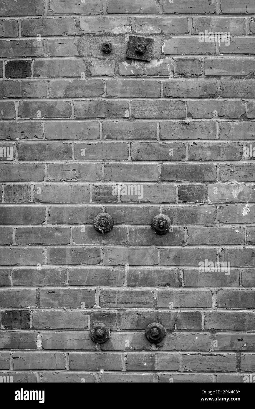 Brick wall with remnants of paint and five iron bolts and washers in black and white. Stock Photo