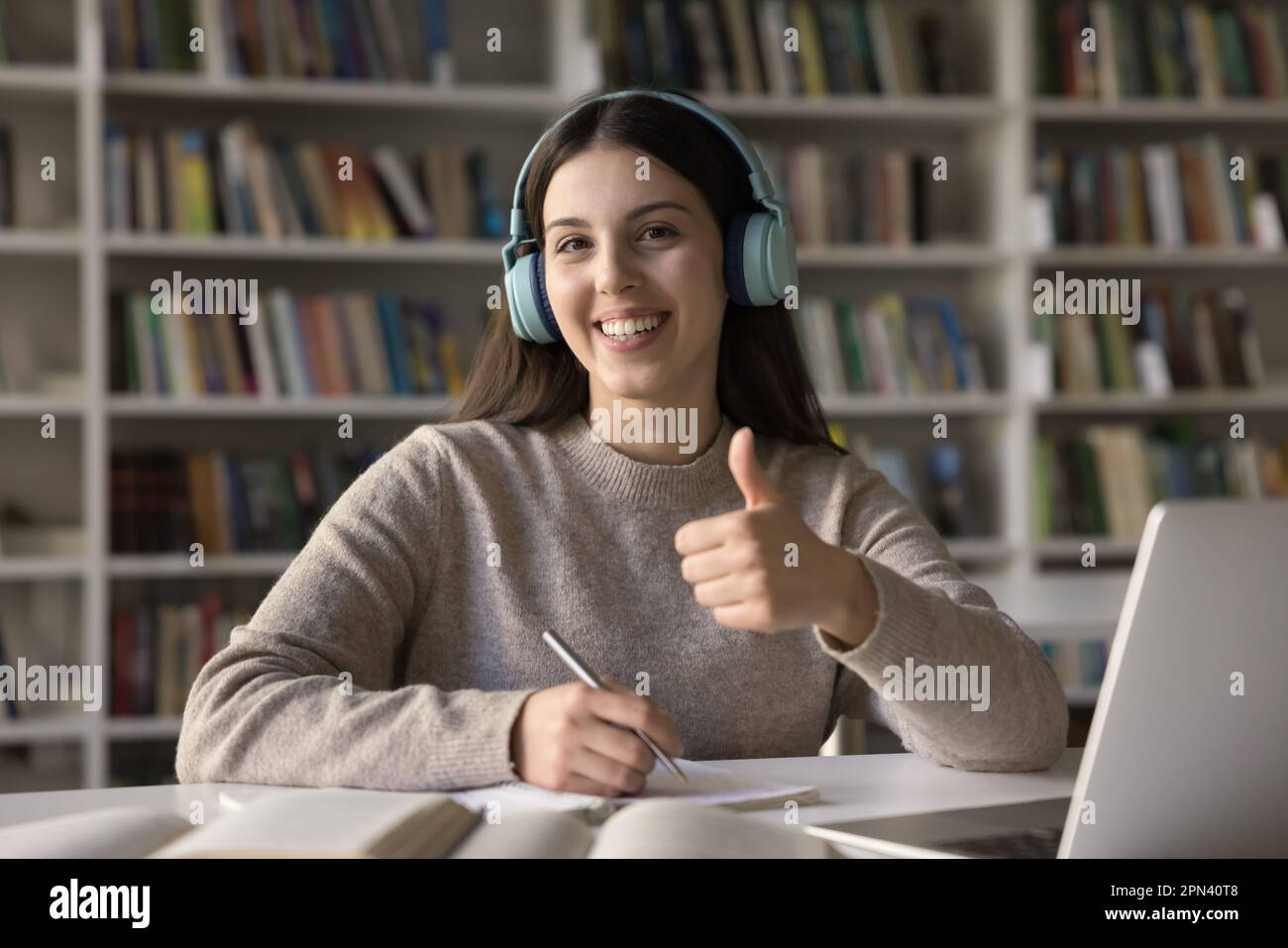 Student girl showing thumbs up seated at desk in library Stock Photo ...