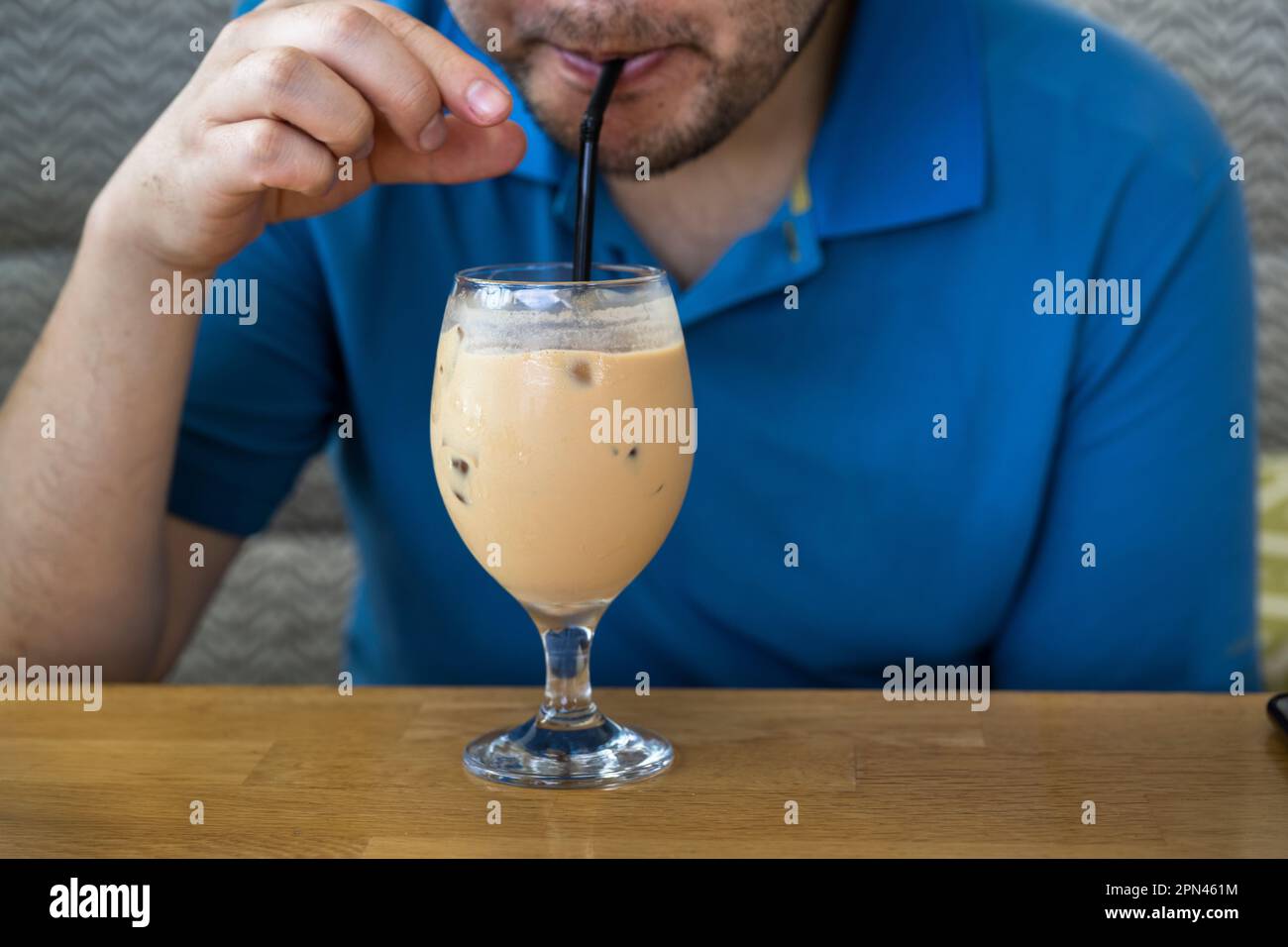 Drinking iced latte coffee with a straw on a wooden table. Cold brew refreshment summer drink. Stock Photo
