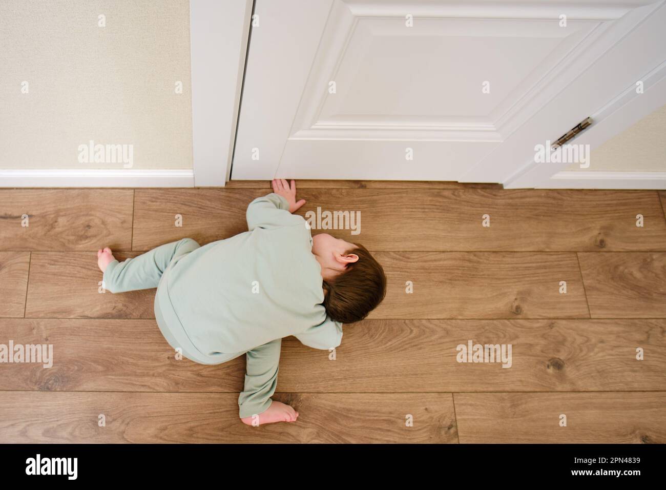 Little baby peeps under the door. Small child looks through the crack