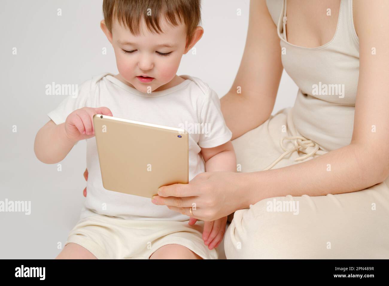 Happy baby with mother looking into digital tablet on studio white ...
