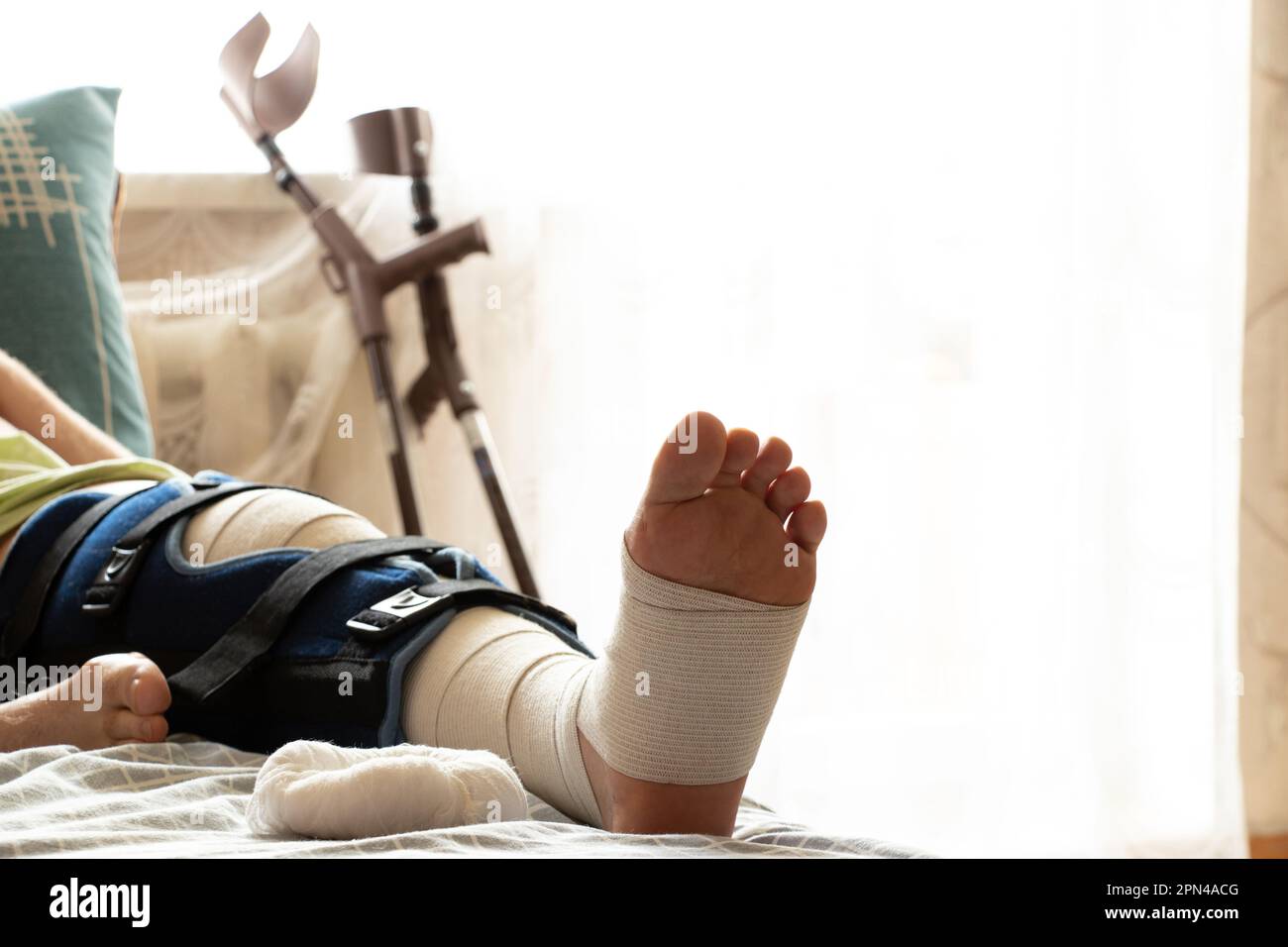 A man lies on a bed after surgery on his knees and crutches next to the