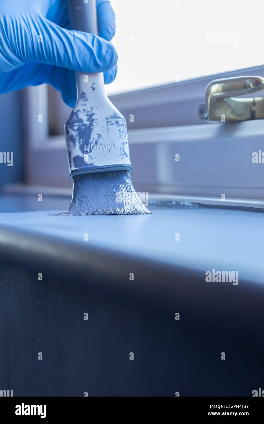 Person painting a window sill with blue paint using a brush. Do it