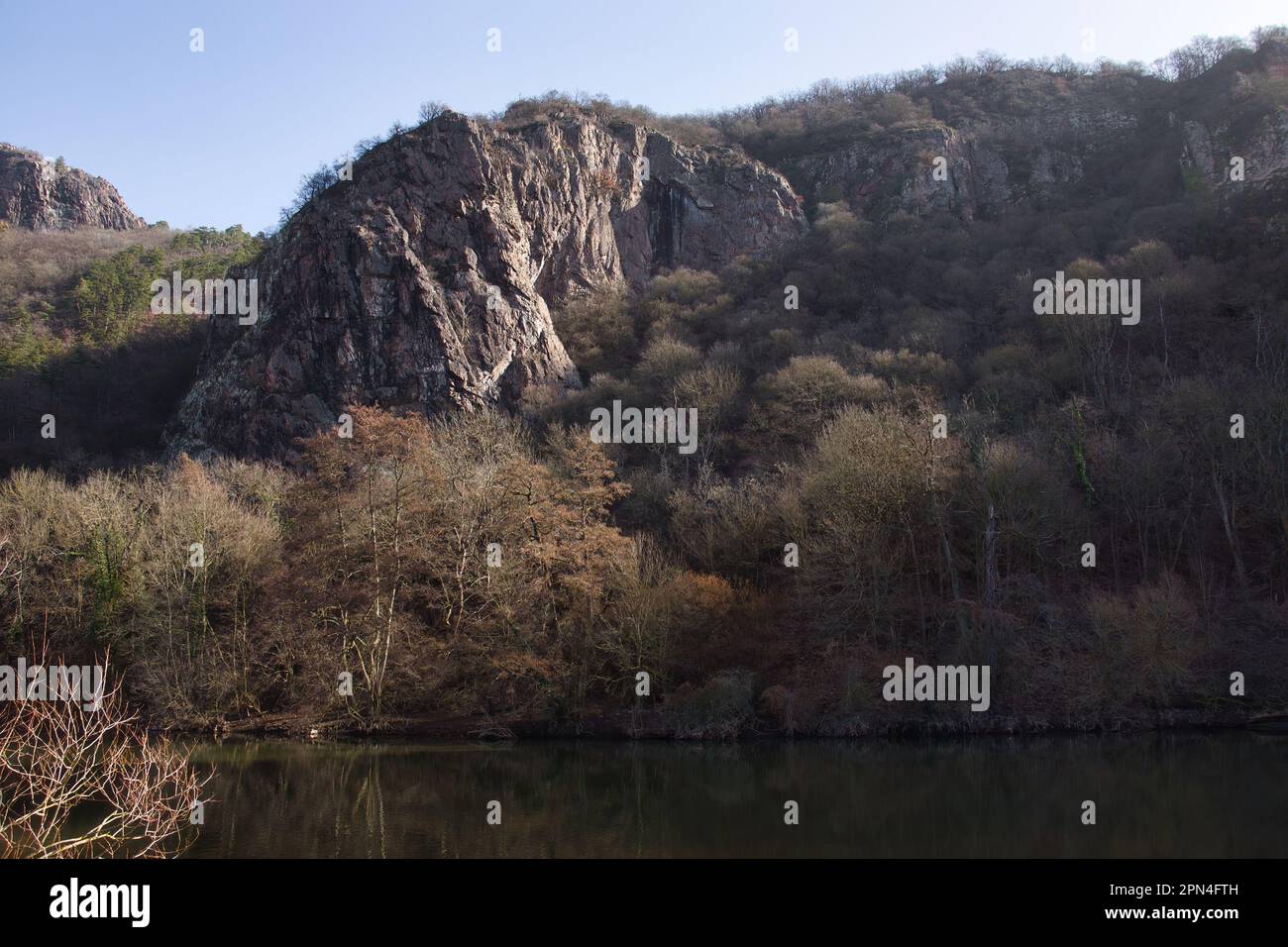 Sun shining on a rock formation in Rotenfels on a hill with trees above the Nahe River on a winter day in Germany. Stock Photo