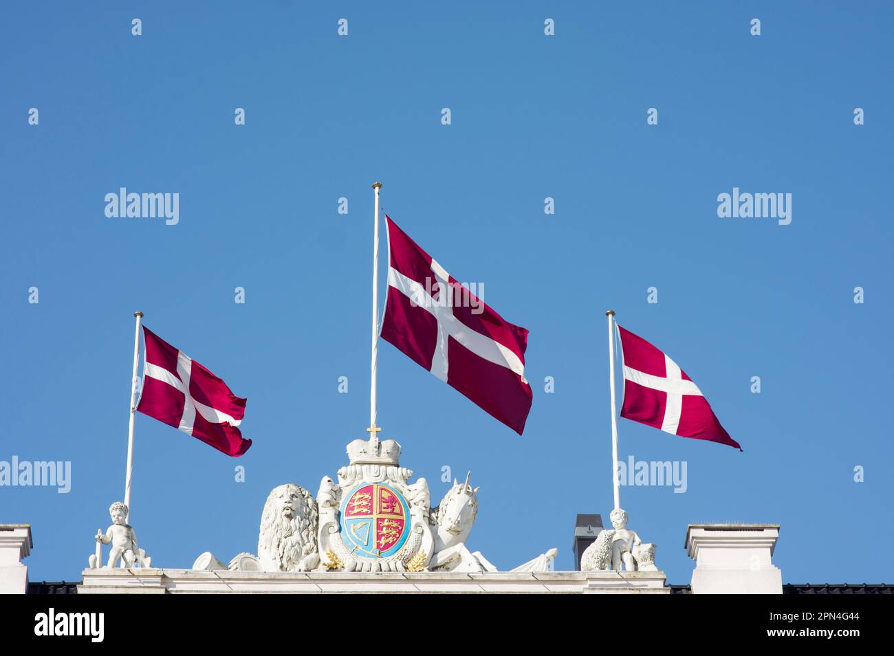 Three danish flags waving in the wind on a nicely decorated historic roof in Copenhagen in Denmark and a clear blue sky Stock Photo
