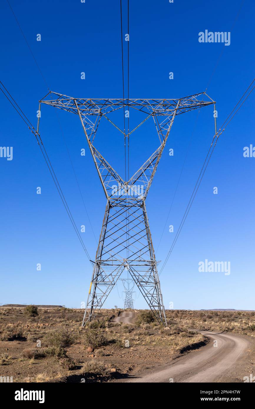 High voltage electricity transmission pylons with a two track gravel road running beneath it in an arid area. Stock Photo