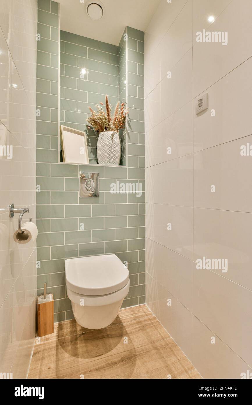 a white toilet in a small bathroom with green tiles on the walls and