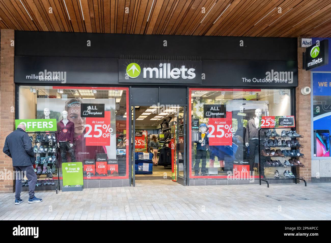 Man browsing in front of Millets shop, business selling outdoor clothing, Bracknell town centre, Berkshire, England, UK Stock Photo