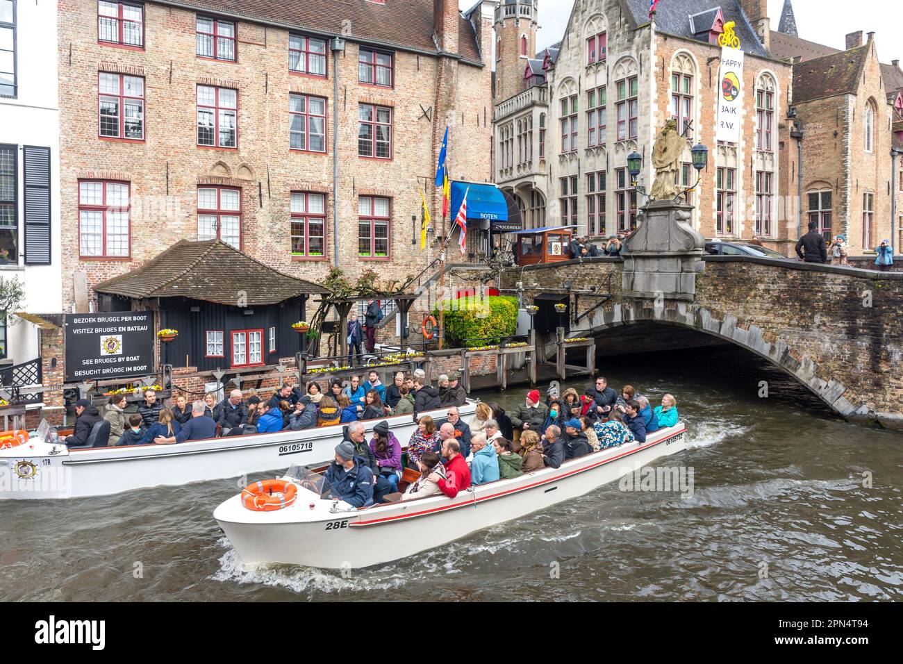 Tourists enjoying a boat tour along a picturesque canal in Bruges, passing by historic buildings and under a stone bridge.