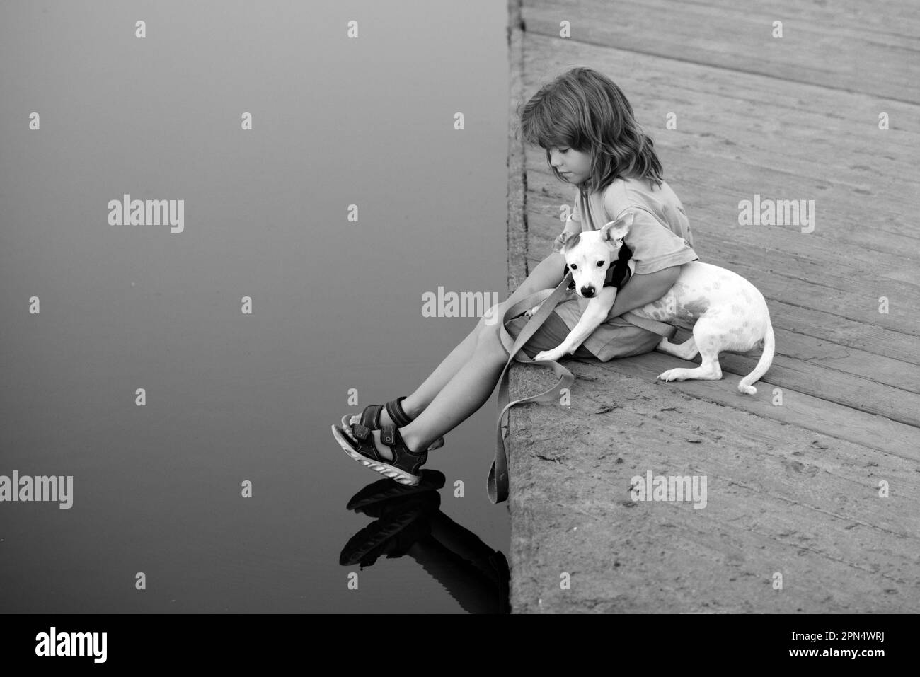 Funny child playing with her puppy dog in the park near lake. Carefree