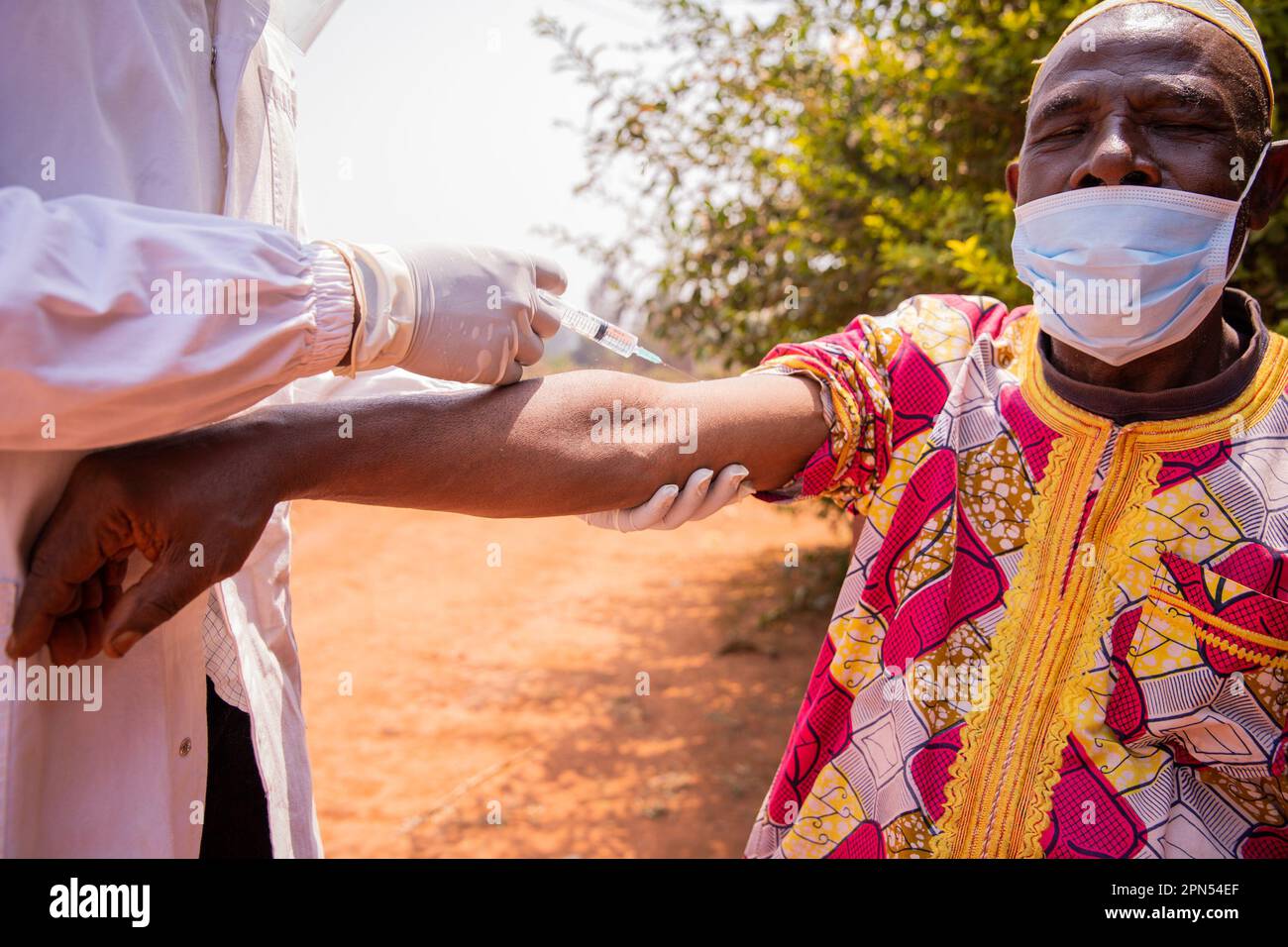 An African doctor vaccinates an elderly man with a syringe on his arm. Stock Photo