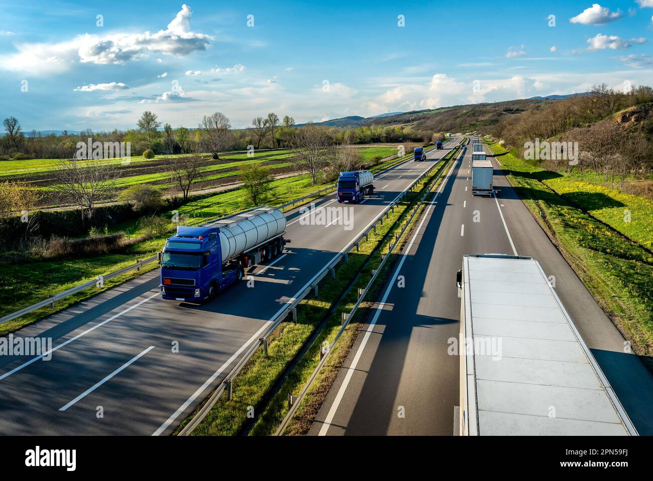 Heavy Highway transportation scene with Convoy of white transportation trucks in one way and blue tank tracks passing in the opposite way on rural hig Stock Photo