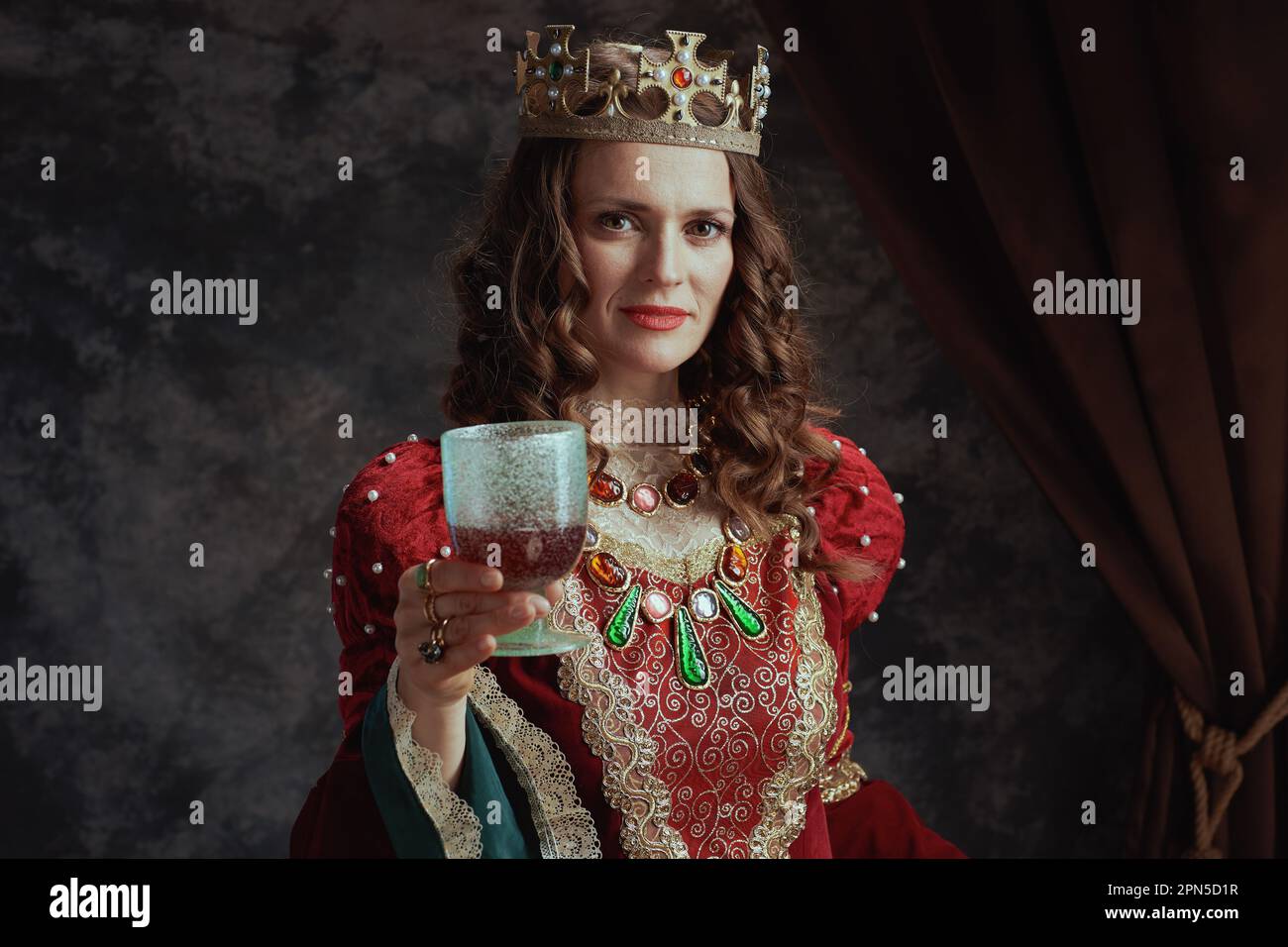medieval queen in red dress with goblet and crown on dark gray ...
