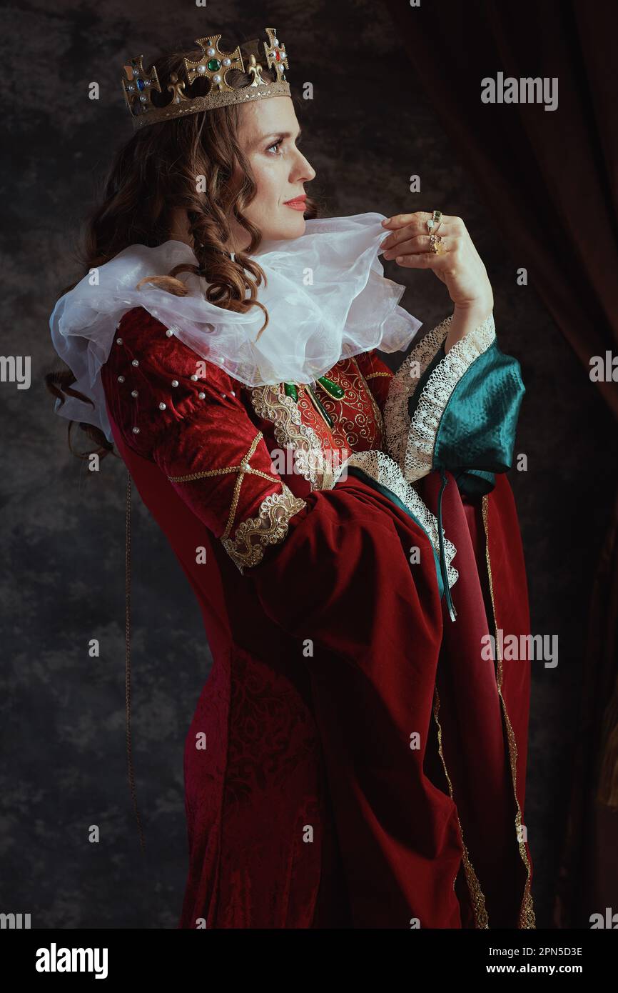 pensive medieval queen in red dress with white collar and crown on dark ...