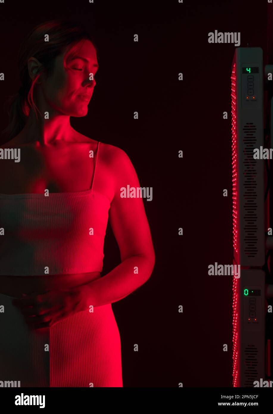 Woman getting red light therapy in a beauty spa. Mature woman standing next to a red light device. Anti-aging and skin care treatment. Stock Photo