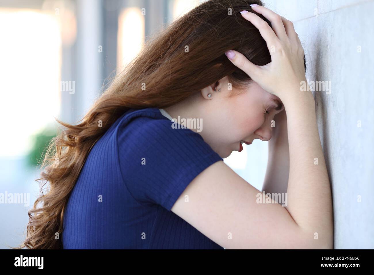 Side view portrait of a sad woman complaining leaning in a wall Stock Photo
