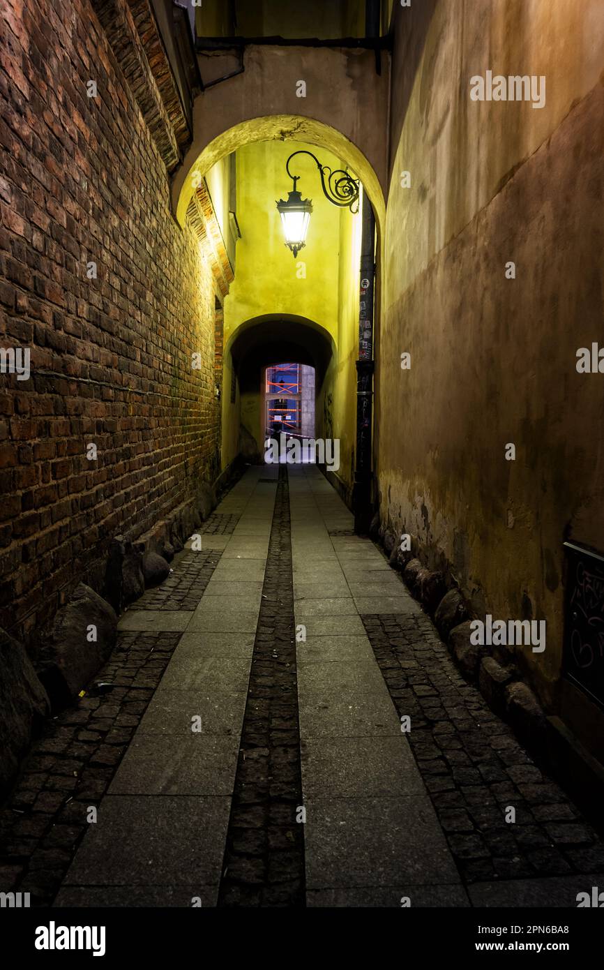 Narrow dark alley illuminated by single lamp at night in the Old Town of Warsaw city in Poland. Stock Photo
