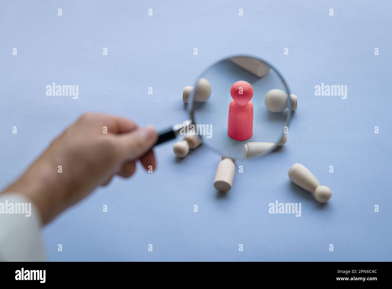 Magnifying glass on red wooden doll with other fallen dolls by the side, Talent search or selection concept. Stock Photo