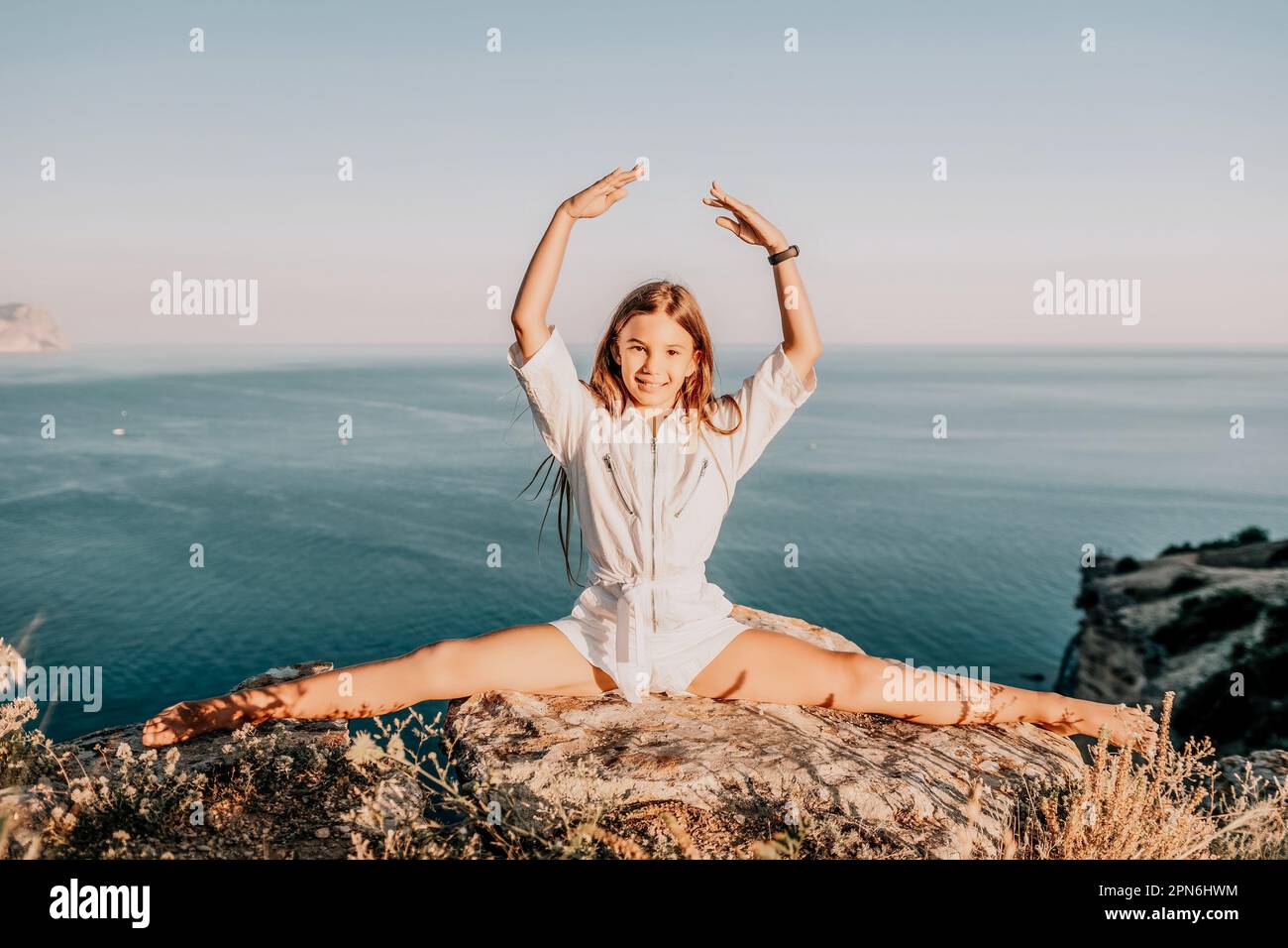 Happy smiling teen girl balerina performs stretching exercises splits on the beach during a