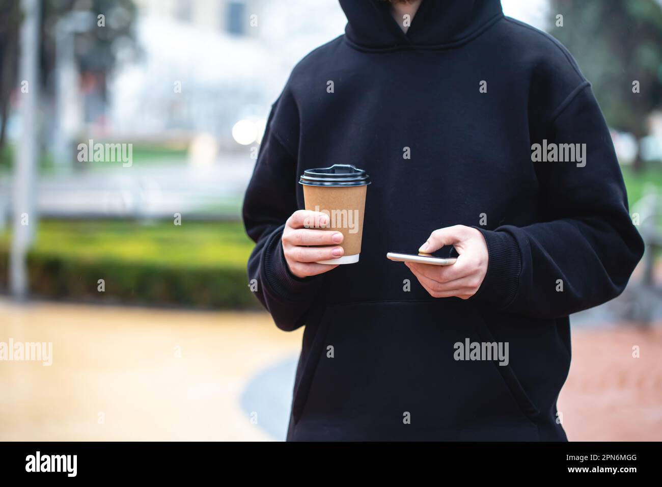 Man holding paper cup and smartphone outdoors. Stock Photo