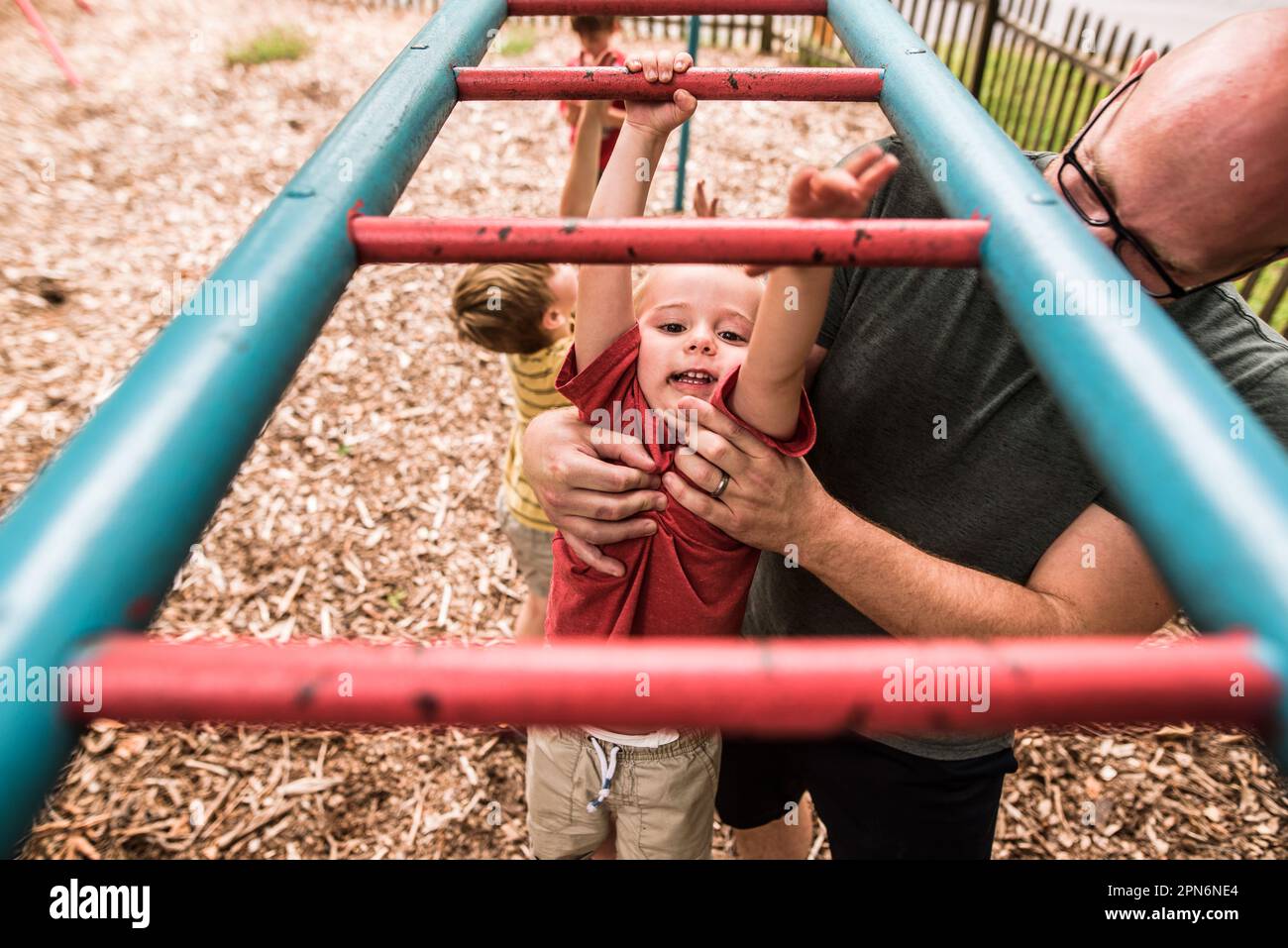 Toddler boy doing monkey bars with help from dad Stock Photo Alamy