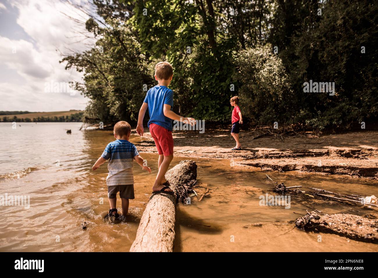 Three boys playing in and around lake on sunny day Stock Photo