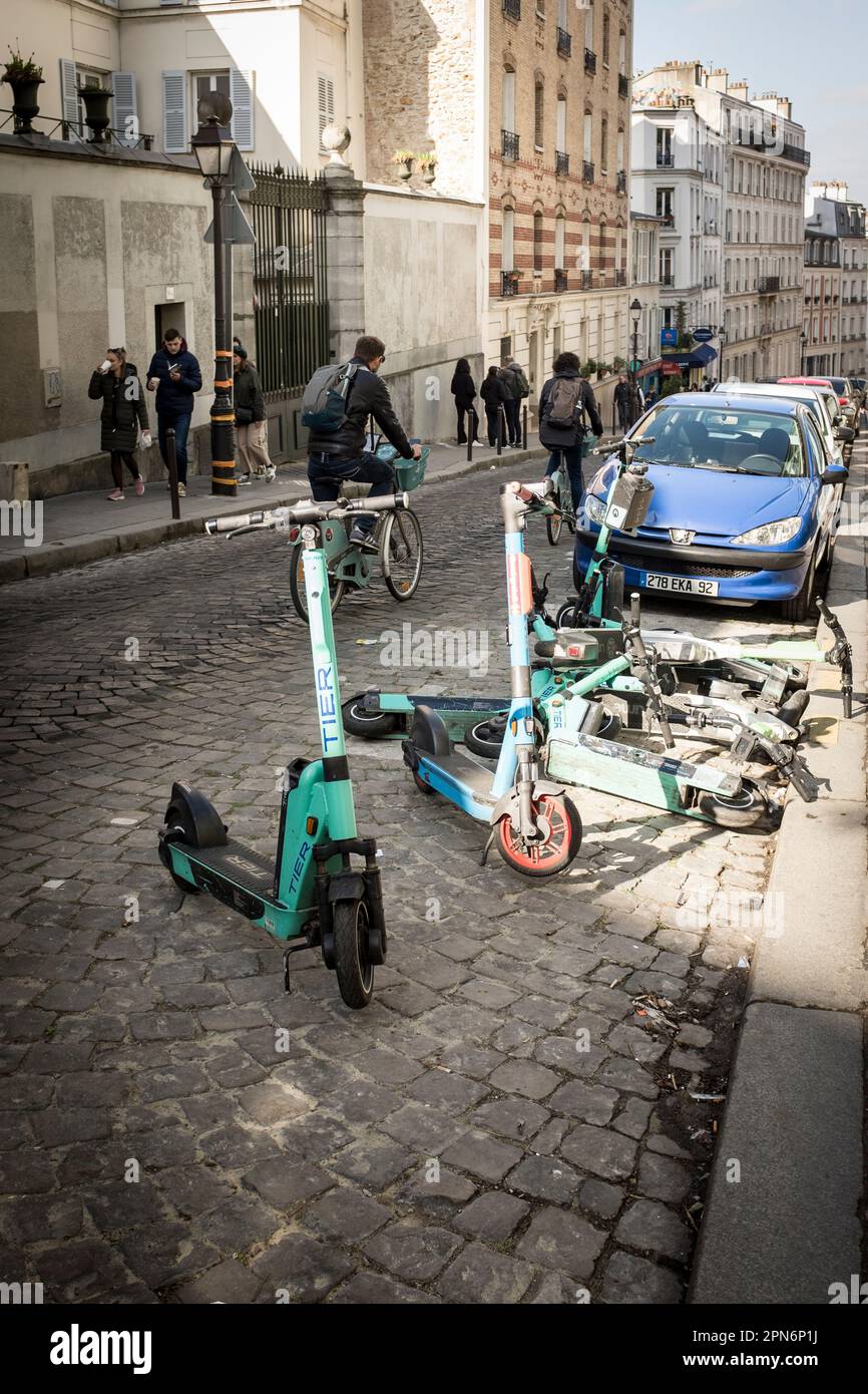 Rental E-scooters from various companies parked and fallen in the narrow cobbled streets of Montmartre, Paris, France. Stock Photo