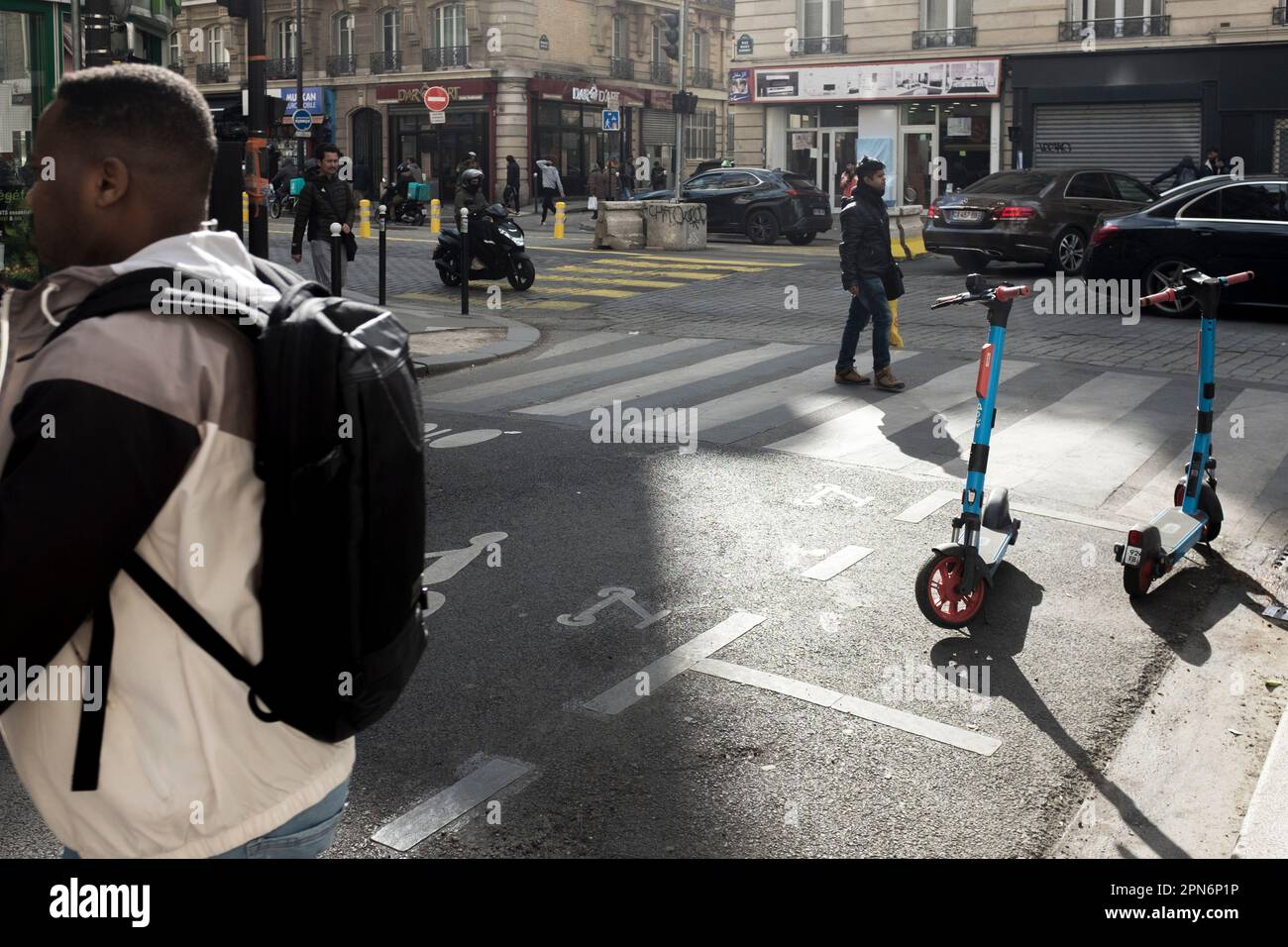 Predestrians walk by Rental e-scooters parked on the road in a designated parking area painted on the ground, in Paris, France. Stock Photo