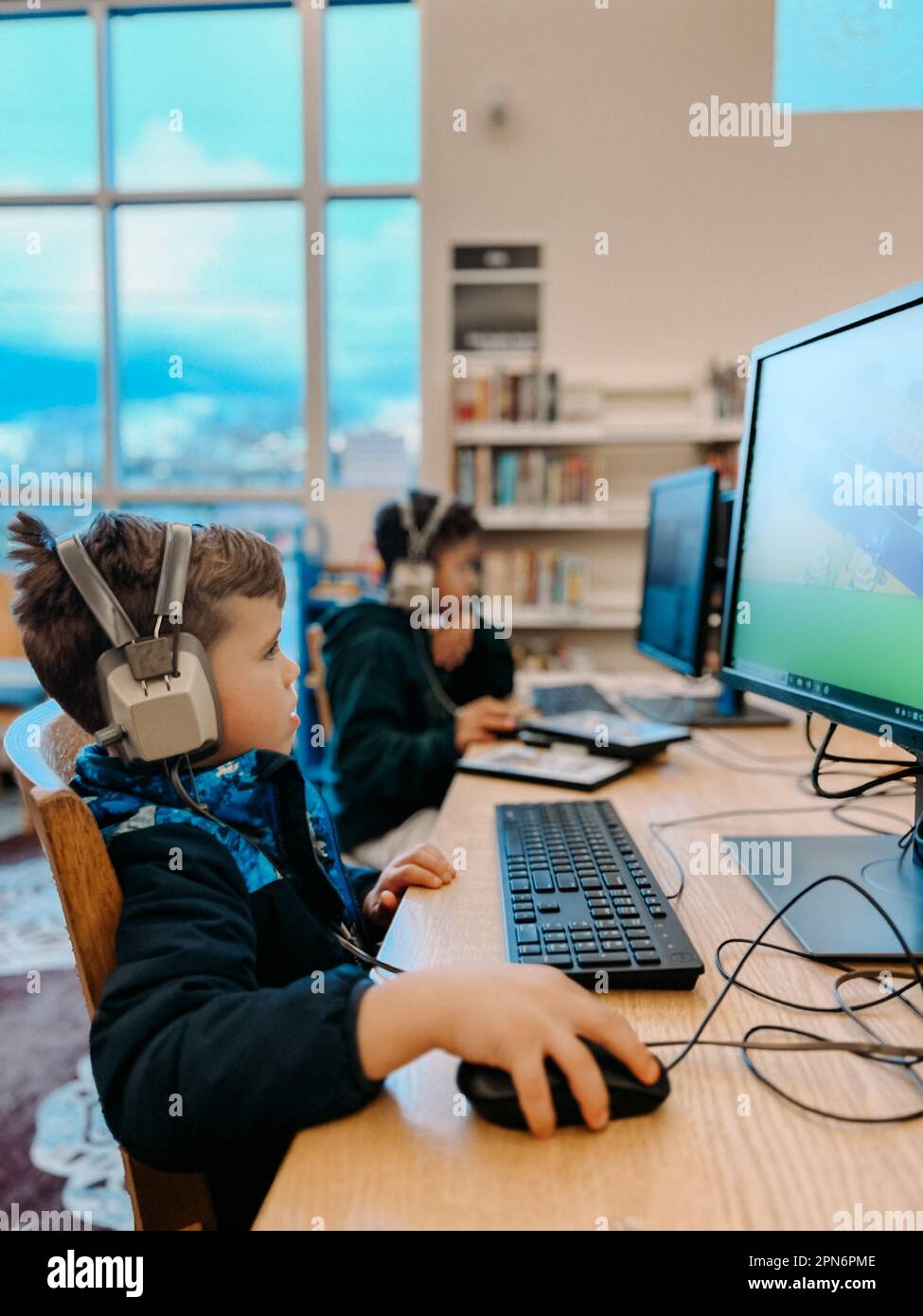 Elementary brothers playing on computers at library with headphones Stock Photo