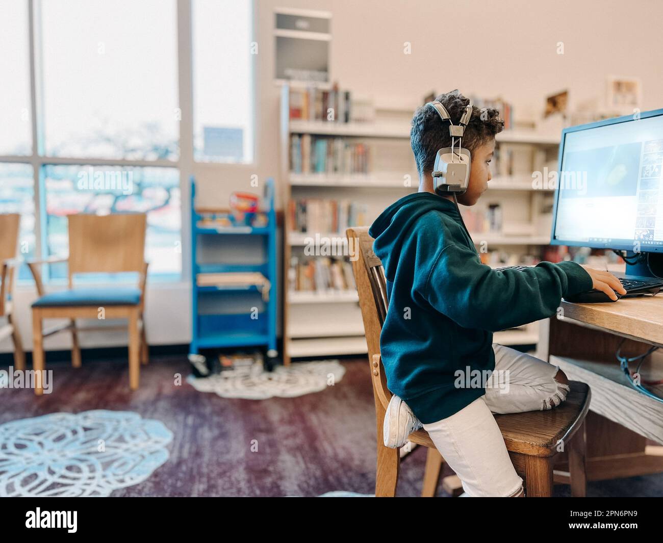 Mixed race boy using computer with bookshelves in background Stock Photo