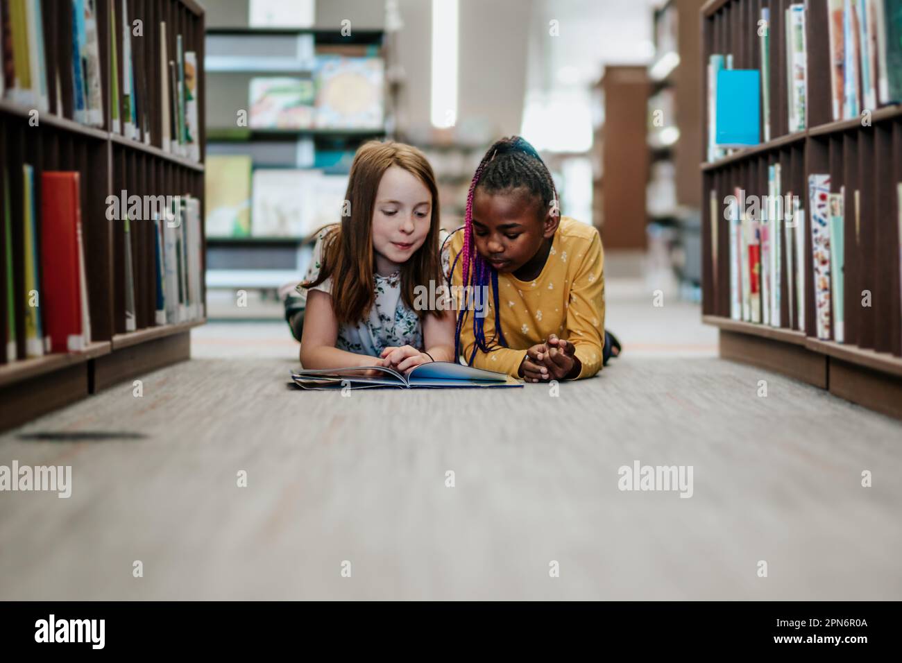 Young girls reading a library book together inside Stock Photo
