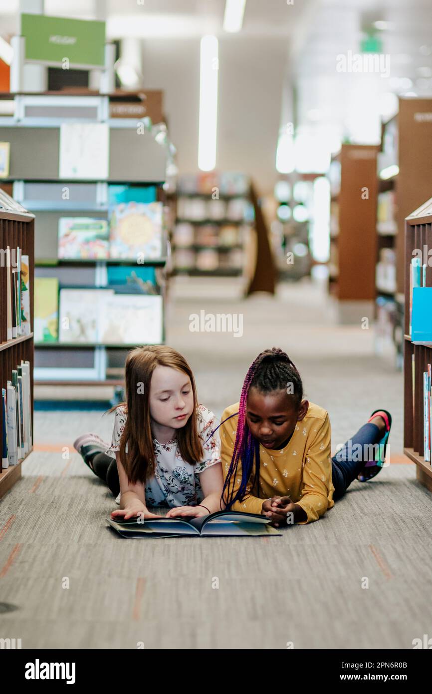 Elementary aged friends reading a book in library Stock Photo