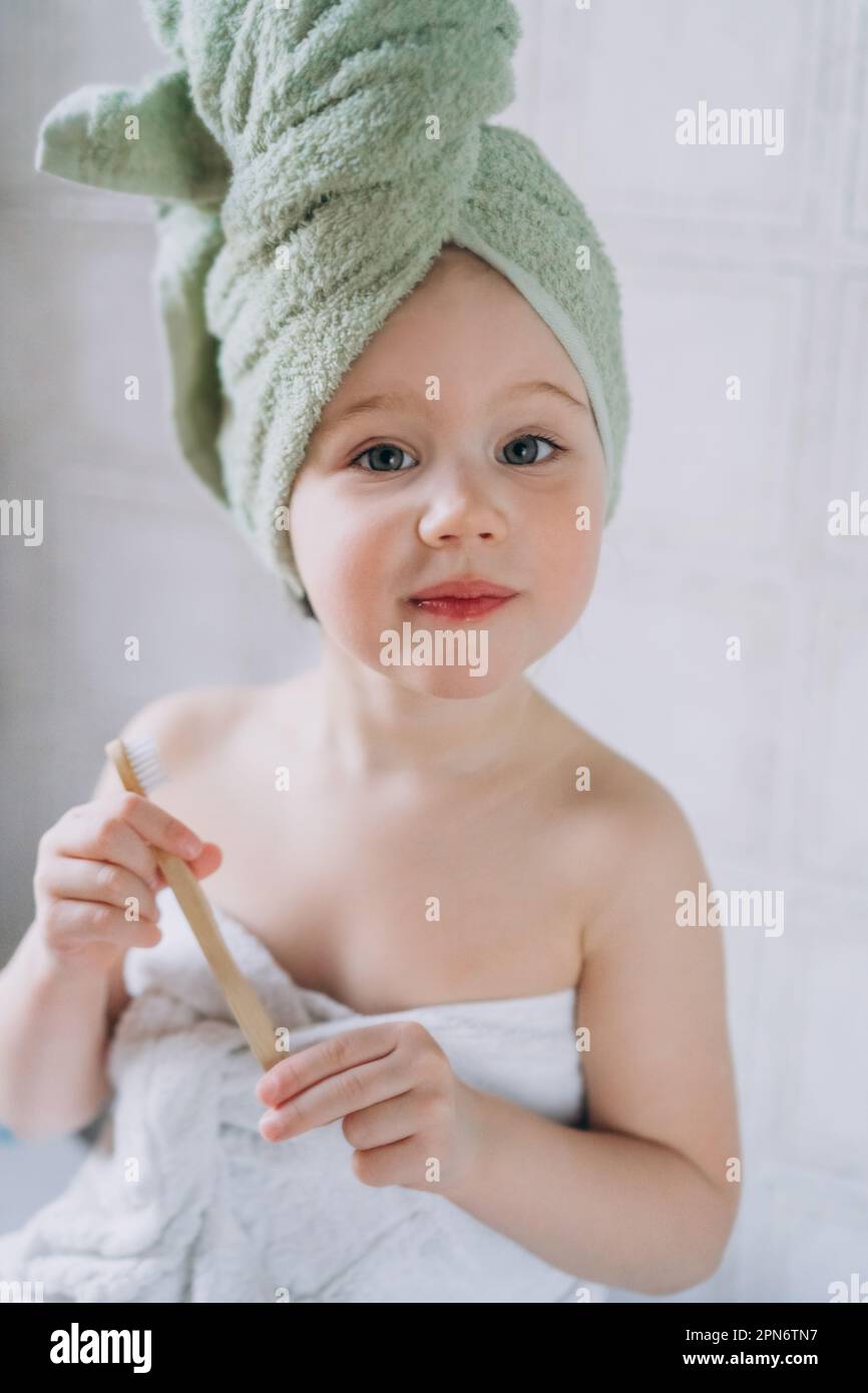 Toddler baby with a towel on her head brushes teeth with brush Stock