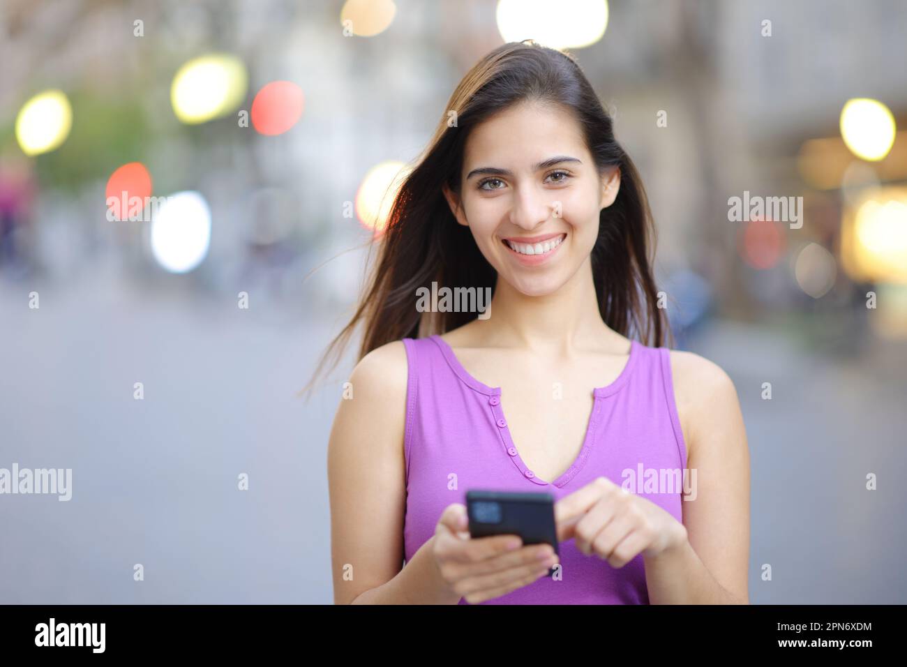 Front view portrait of a happy woman holding smart phone in the street looking at you Stock Photo