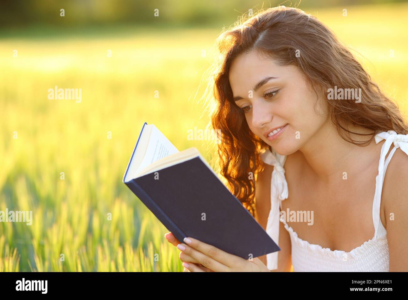 Happy woman sitting in a field reading a paper book at sunset Stock Photo