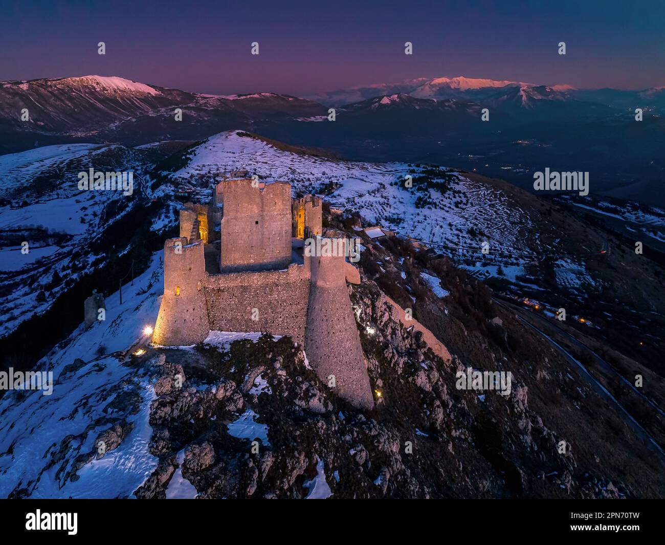 Aerial view of the Rocca di Calascio with snow and lit by the light of the sunset, in the background the mountains of the Maiella National Park. Stock Photo