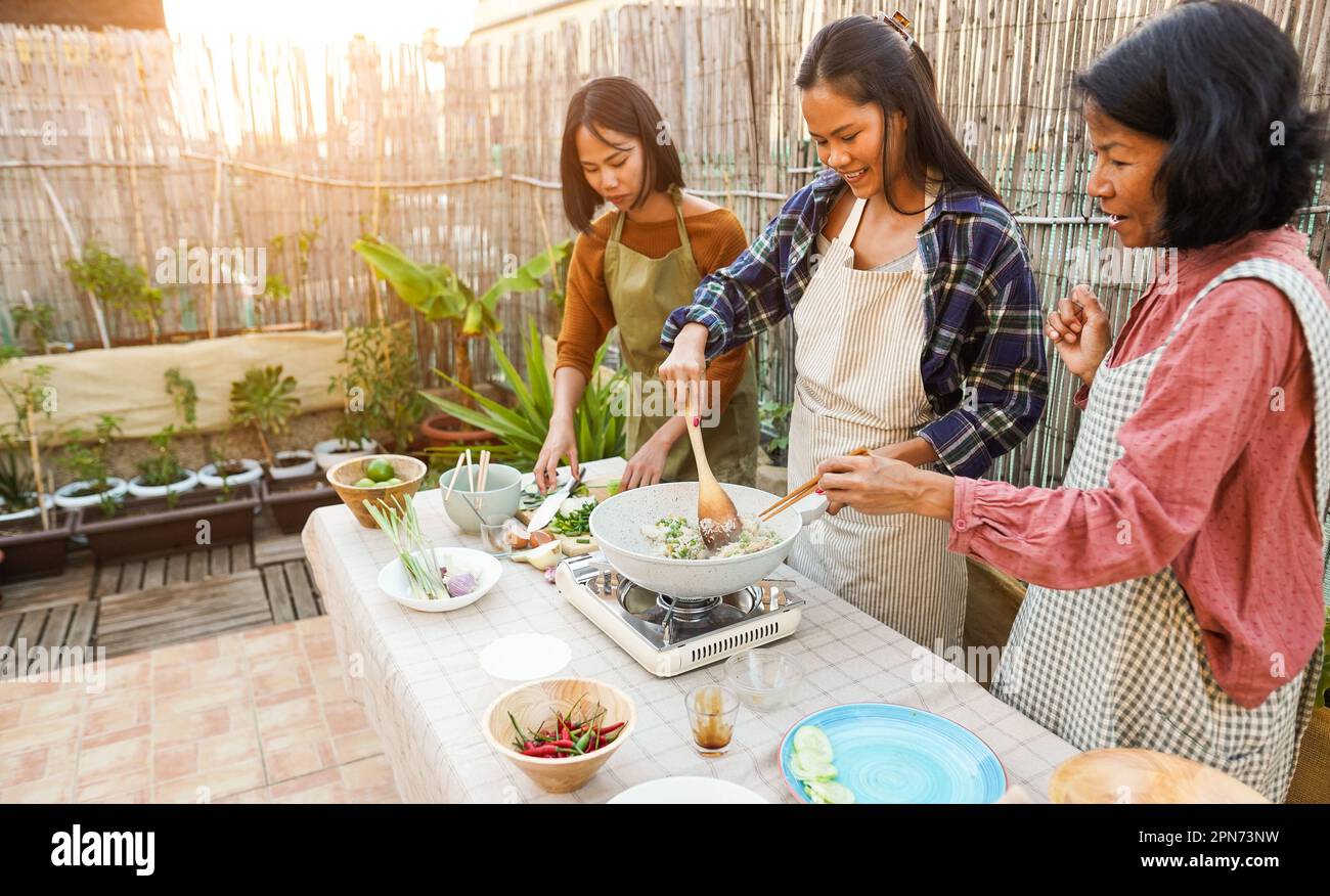 Asian family cooking together at home outdoor - Mother and two daughters having fun preparing dinner at house backyard - Main focus on center girl Stock Photo
