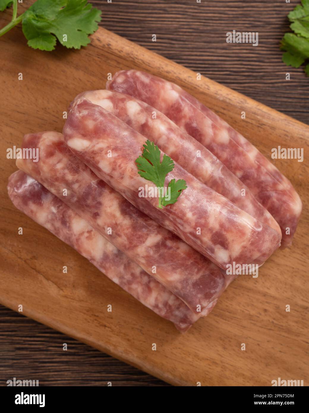 Raw Taiwanese sausage in garlic flavor with garlic cloves in a plate on wooden table background. Stock Photo